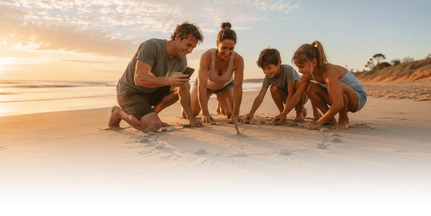 A family on a beach at golden hour building a sundial in the sand — a leaning stick as the gnomon and stones marking the hours around a drawn circle — checking a phone as they work.
